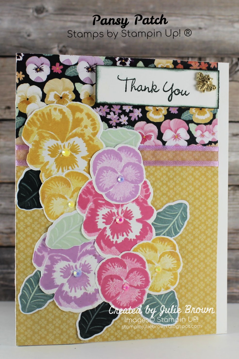 Card designed with Pansy Patch Stamp set.  Avid Card with two different Designer Series paper as back ground with ribbon wrapped around where they meet together then Stamped pansies and leaves cut out with dies and then layered onto the card staring at top and layering down left side of card.